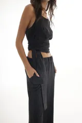 Top negro con acabado brillante, de tirantes finos y diseño cruzado en la cintura con lazo lateral ajustable.