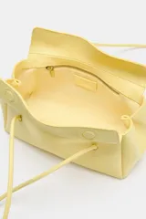 Bolso de hombro en formato alargado color amarillo pastel, con doble asa fina de hombro, bolsillo interior con cremallera y cierre imantado.