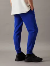 Pantalón de chándal azul eléctrico de felpa de algodón regenerativo, con cintura elástica con cordón, puños de canalé, bolsillos laterales y trasero, y logo de Calvin Klein en relieve en la cadera.