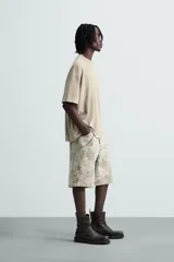 Bermuda relaxed fit de algodón, color beige con estampado abstracto en tonos grises. Cuenta con cinco bolsillos y cierre frontal de cremallera y botón.