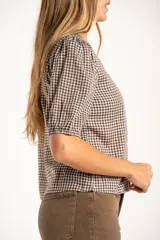 Blusa de algodón con estampado de cuadros vichy en tonos negro y blanco. Presenta escote en V, cierre frontal con botones y mangas cortas abullonadas con terminación elástica.