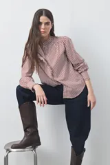Camisa de manga larga a rayas verticales en tonos blanco y bordó, con cuello alto y detalle de volados frontales. Presenta puños con volados y un corte fluido.