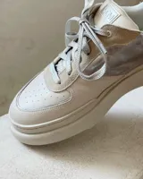 Championes urbanos de plataforma, combinando cuero texturizado en tono crema, detalles en gamuza beige y paneles laterales en cuero metalizado plateado. Presentan cordones planos plateados y suela de goma al tono.