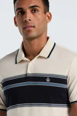 Polo de manga corta Original Penguin confeccionada en tejido interlock, color beige con franja horizontal central en azul marino y detalles en celeste. Presenta cuello clásico con botones y logo bordado en el pecho.