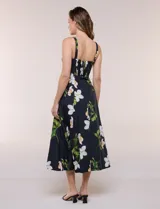 Vestido midi evasé de algodón color negro con estampado floral blanco y verde, de la marca Julia Jordan. Presenta escote recto, breteles anchos y espalda en punto smock. Incluye bolsillos laterales y forro interior de poliéster.