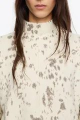 Jersey corto de corte boxy confeccionado en mezcla de lana, con cuello alto y mangas largas rectas, de color beige con diseño estampado tipo efecto salpicado en tonos gris y marrón.