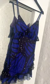 Vestido corto con estampado de mariposas azules y negras, escote en V con volantes y tirantes finos.
