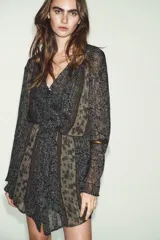 Vestido corto con estampado floral en tonos azul oscuro y beige, con detalles en hilo metalizado. Presenta escote pico con cordón ajustable terminado en borlas, mangas largas acampanadas y cintura elástica ajustable.