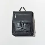 Mochila negra de cuero sintético con textura croco en el bolsillo frontal. Tiene cierre superior con cremallera y hebilla decorativa.