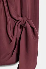 Top fluido sin mangas, de color bordó, con escote en V cruzado y detalle de nudo drapeado en el lateral delantero.