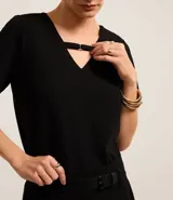 Blusa negra de crepé con cuello en V y mangas cortas. El cuello posee una tira horizontal unida por una pequeña hebilla metalizada.