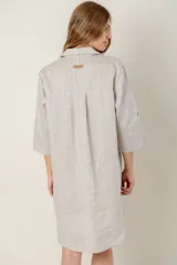 Vestido camisero corto de lino color celeste, con cuello clásico, cierre frontal con botones, mangas 3/4 con trabillas y bolsillo de parche en el pecho con bordado de iniciales.