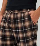 Pijama masculino compuesto por una remera negra de manga corta con cuello henley y botones, y un pantalón largo con estampado de cuadros en tonos marrones, negros y blancos.