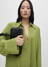 Camisa de gasa color verde oliva, de corte oversize y diseño recto. Presenta cuello camisero con escote en V profundo, mangas largas con puños y bajo con aberturas laterales.