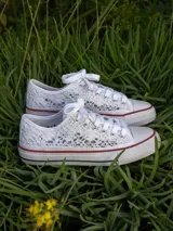 Zapatillas bajas de lona blanca con detalles de encaje bordado y suela de goma con líneas rojas y negras.