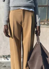 Pantalón de vestir color tostado con diseño de corte recto y tiro medio. Presenta detalle de pinzas frontales, trabillas para cinturón y cierre oculto con cremallera, botón y ganchos.
