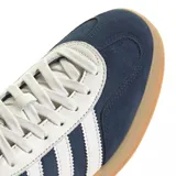 Championes adidas Gazelle de diseño clásico, confeccionados en gamuza azul con las icónicas tres tiras laterales en blanco. Presentan detalles en blanco en el talón y la lengüeta, con el nombre del modelo en dorado y una suela de goma color caramelo.