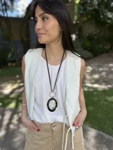 Collar largo con cordón de cuero negro, dije ovalado de guampa engarzado en alpaca plateada y aro plateado.