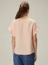 Blusa de lino color rosado, de corte recto y holgado, con cuello redondo y mangas cortas adornadas con volados.