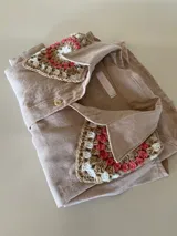 Camisa tostada de manga larga con cuello clásico decorado con apliques de crochet en tonos marrones, blancos y verdes, cierre frontal de botones y diseño holgado.