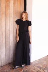 Pantalón de lino negro con silueta amplia y fluida, tiro medio y bordado artesanal sutil en la parte inferior de una de las piernas.