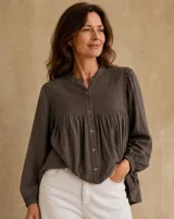Camisa manga larga color marrón oscuro, con cuello mao y cierre frontal con botones. Presenta detalles de fruncidos tipo nido de abeja en el pecho y los hombros, y puños elásticos.