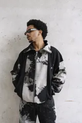 Campera unisex de cuello alto con cierre frontal completo. Presenta un diseño de paneles con efecto de lavado ácido en tonos negro y gris, corte relajado y bolsillos laterales.