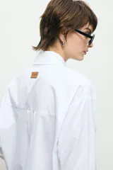 Camisa blanca de corte oversize, con cuello clásico, cierre frontal con botones y mangas largas.
