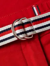 Pantalón chino rojo de corte slim, con cierre de botón y cremallera, y diseño de 4 bolsillos. Incluye un cinturón de tela a rayas blancas y azules con hebilla metálica.
