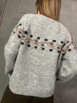 Saco cardigan gris de punto con detalles en tonos chocolate y diseño estampado en la parte superior y mangas. Cuenta con cierre frontal de botones y ribetes marrones en los bordes.