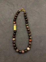 Collar de cuentas de piedras naturales en tonos tierra, con detalles de tubos dorados en los laterales.