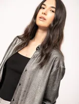 Camisa oversized con terminación metalizada color gris plomo. Tiene botones a tono en el delantero, largo por debajo de la cadera y tajos a los costados.
