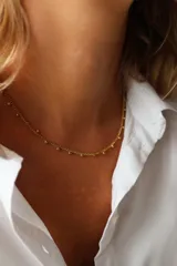 Gargantilla delicada de acero dorado con pequeñas esferas distribuidas a lo largo de la cadena.