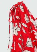 Vestido largo de tejido fluido con escote en pico cruzado y diseño evasé. Presenta tirantes anchos con detalle de lazos ajustables en los hombros y estampado floral en tonos rojos y crema.