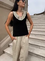 Top negro de cuero con escote en V y apliques de caracoles cosidos a mano en el escote.