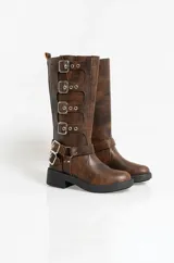 Borcegos de caña alta confeccionados en cuero sintético con acabado envejecido. Presentan múltiples hebillas metálicas decorativas a lo largo del lateral y una correa ajustable con hebilla doble en la zona del tobillo. Cuentan con suela de goma negra con plataforma y cierre lateral.