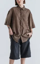 Camisa de corte oversize y mangas cortas, confeccionada en tejido con efecto desgastado color marrón chocolate. Presenta cuello clásico, cierre frontal con botones y diseño holgado.