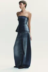 Jeans de tiro alto, color azul medio lavado, con un corte extremadamente ancho y voluminoso (balloon/oversize). Presenta costuras torcidas y paneles de denim de tono ligeramente diferente en los laterales, creando un efecto visual dramático.