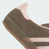 Championes Adidas Gazelle Indoor de diseño clásico, confeccionados en gamuza color marrón con las icónicas tres tiras laterales y refuerzo en el talón en color rosado. Presentan suela de goma translúcida y cierre de cordones.