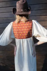 Túnica de lino color beige, de corte midi y diseño holgado, con mangas cortas y pechera combinada con tela estampada y detalles de flecos y botones.