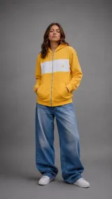 Campera con capucha y cierre frontal, de color amarillo con una franja horizontal blanca en el pecho. Presenta un pequeño logo bordado en el frente y bolsillos tipo canguro.