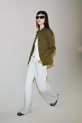 Chaqueta de estilo utilitario color verde militar, con cuello solapa, manga larga y cierre frontal con botones ocultos por solapa. Presenta bolsillos con solapa en la parte delantera y un bolsillo de plastrón en el pecho.