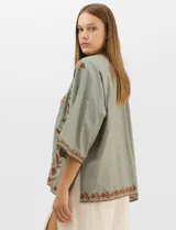 Cardigan tipo kimono de color verde con bordados florales en tono marrón a lo largo de los bordes frontales y en las mangas. Presenta un corte amplio y fluido con mangas tres cuartos.