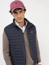 Chaleco acolchado de hombre en color azul marino, con cierre frontal de cremallera, cuello alto y logo engomado en el pecho. Cuenta con bolsillos laterales con cierre y sisa elástica.