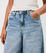 Pantalón de jean con corte barrel, de tiro medio y piernas anchas. Presenta un lavado marmorizado, trabillas en la cintura, cierre frontal con botón y cremallera, bolsillos funcionales y recortes decorativos en las rodillas.