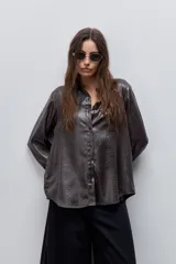 Camisa blanca de calce relajado con acabado satinado y brillo sutil, cuello clásico, cierre frontal con botones y mangas largas con puños.