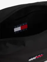 Cartera tipo bandolera de diseño compacto, color negro, con cierre superior y parche con el logo de la marca en el frente.