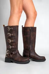 Borcegos negros de caña alta confeccionados en cuero sintético, con hebillas plateadas en los costados y cierre lateral. La altura de la caña es de 33,5 cm y la base mide 5 cm.