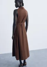 Vestido midi marrón sin mangas, de corte evasé y diseño estilo camisero con cuello clásico, cierre frontal con botones y cinturón ajustable con hebilla.