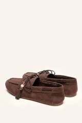 Mocasín estilo náutico de gamuza marrón, con cordones de cuero, borla decorativa y cuentas de colores en el empeine.